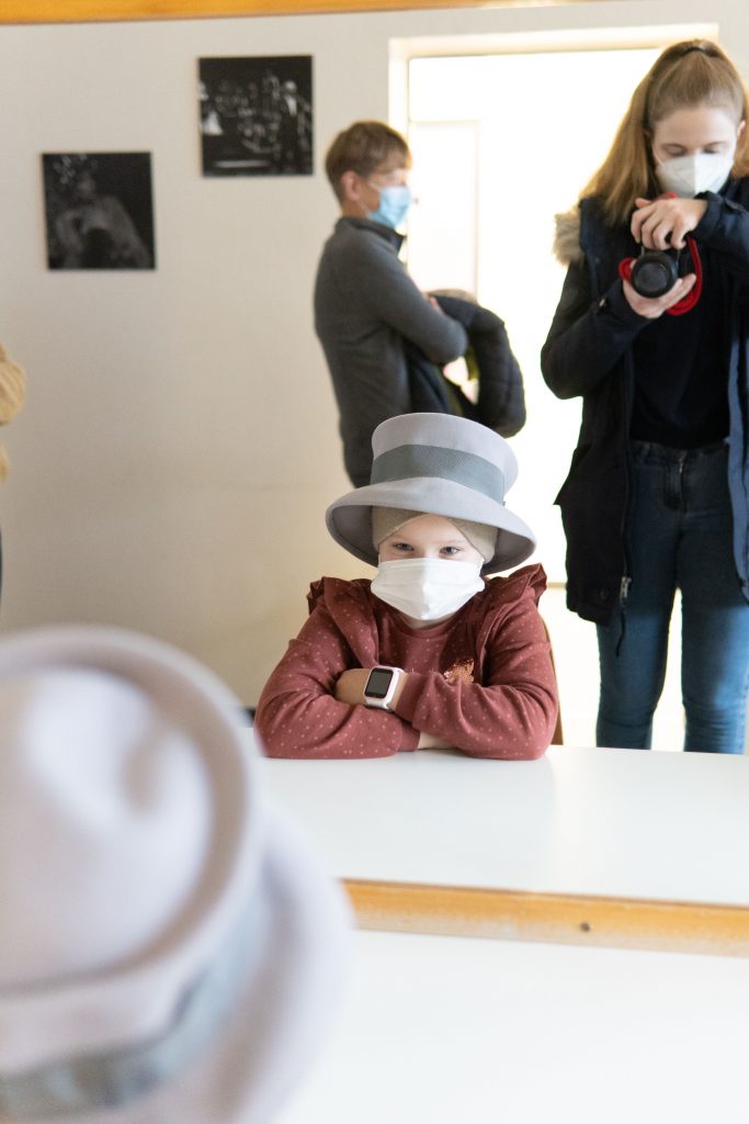Ein Kind trägt einen Hut und sitzt vor dem Spiegel in einer Theatergaderobe.