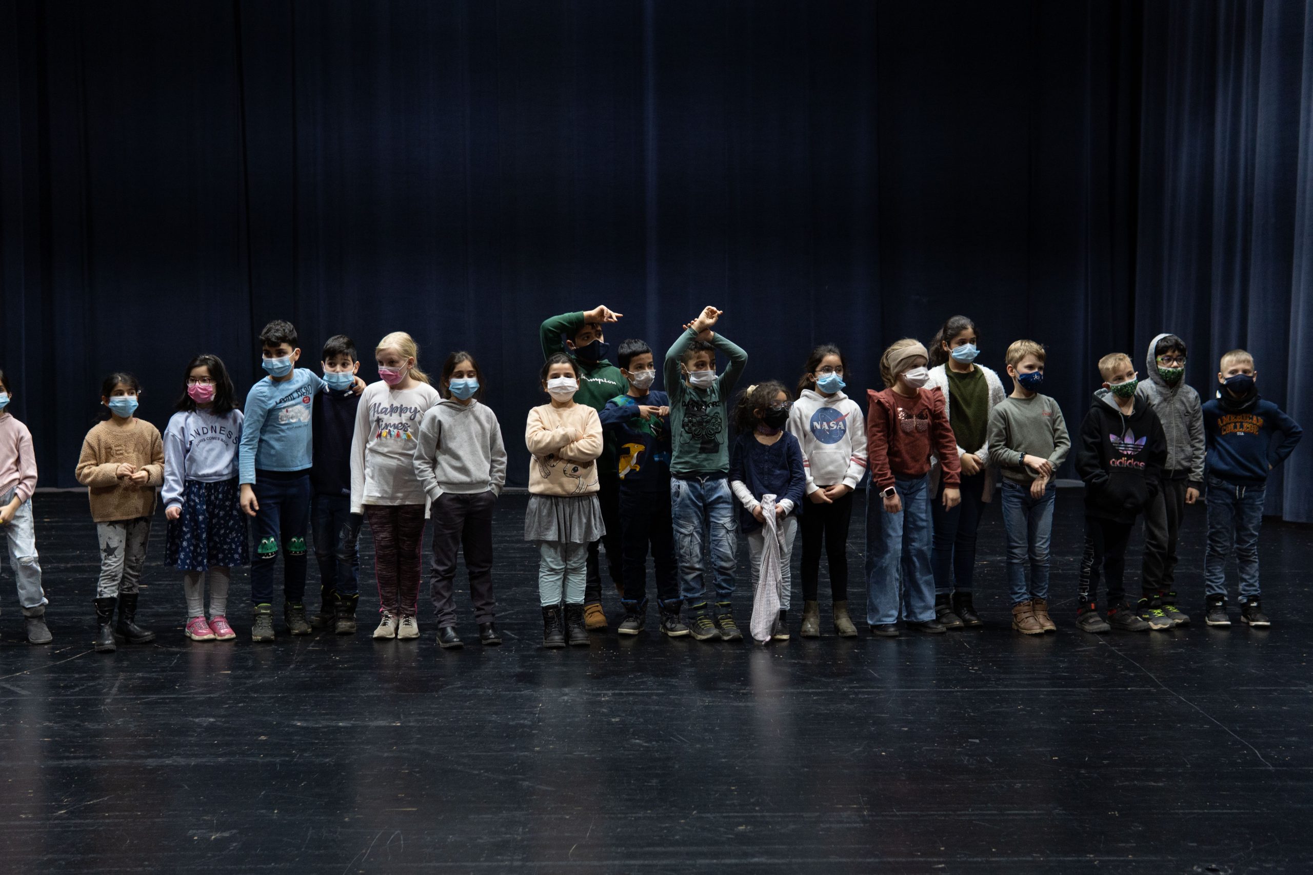Eine Gruppe von 19 Kindern steht in einer Reihe auf einer Bühne.