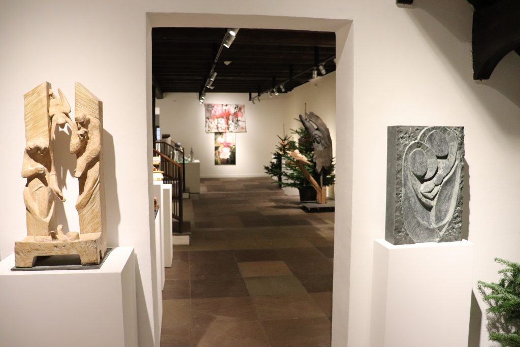 Blick durch einen Durchgang im Museum. Auf der linken und auf der rechten Seite stehen auf jeweils einem Sockel abstrakte Darstellungen der biblischen Krippensituation.