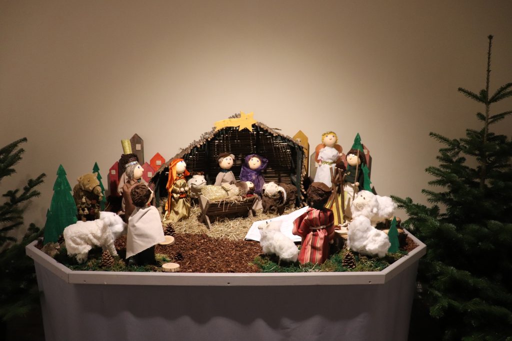 Darstellung der Krippensituation aus der biblischen Weihnachtsgeschichte auf einem Tisch. Es gibt verschiedene Figuren, wie Schafe, Hirten und Engel.